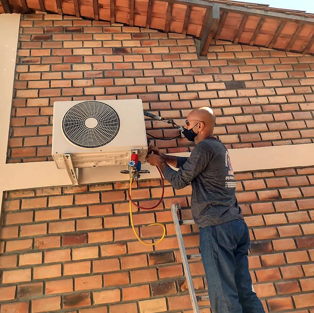 Técnico instalando a condensadora de um ar-condicionado em parede de tijolos